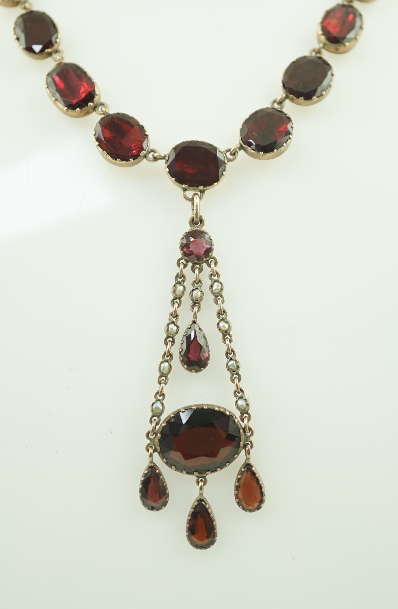 An early 19th century gold, and thirty five graduated foil backed garnet set necklace, with later garnet and seed pearl set drop